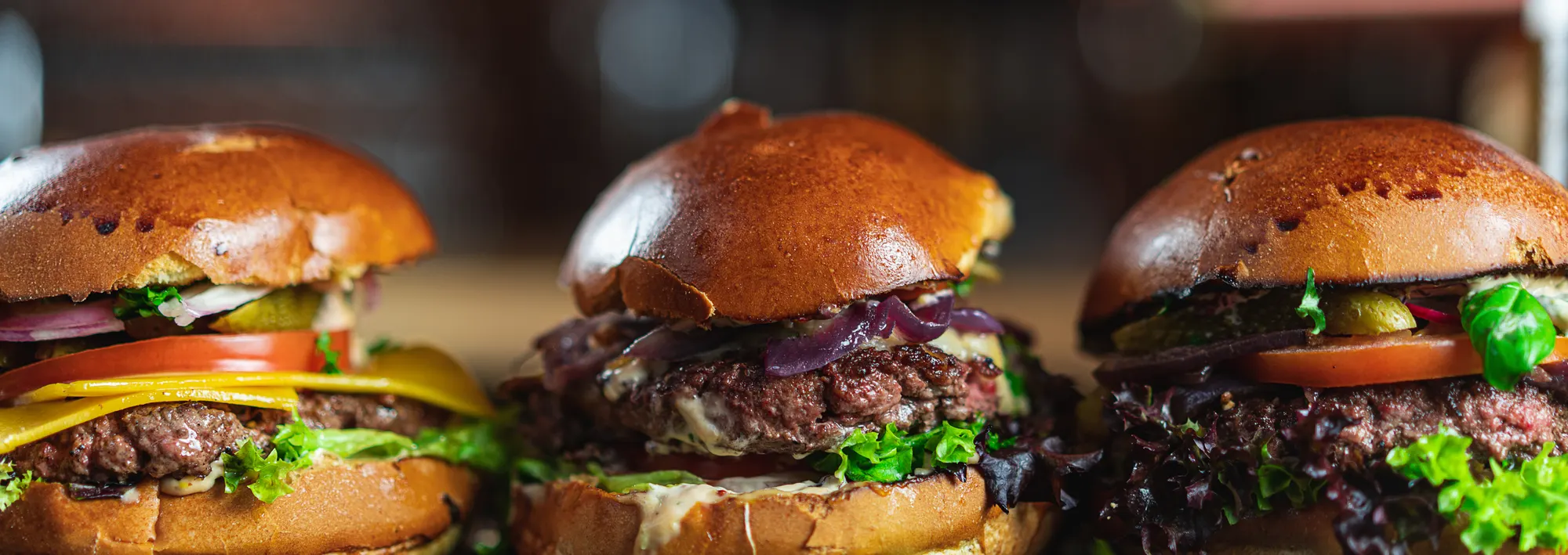 Drei frisch zubereitete Broderick-Burger mit Brioche-Bun nebeneinander auf dem Tresen