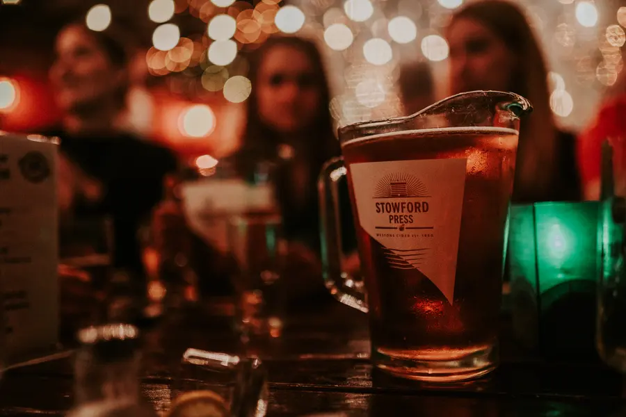 Gäste stoßen im Broderick mit Shots an, im Hintergrund Lichterketten
